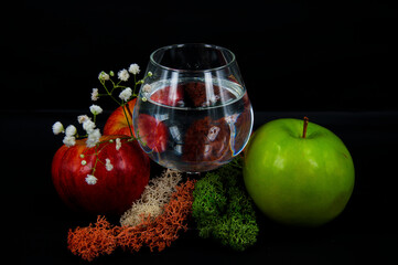art photo glass of water red and green apples moss different color white flowers on a black background