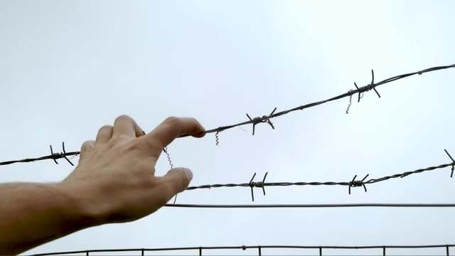 Man hand grabs and pushes the barbed wire fence, close-up