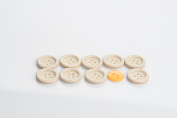 A single out yellow button among white buttons,shot from top over a clear white surface