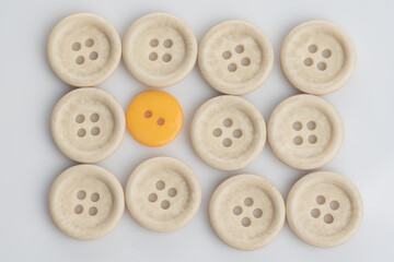 A single out yellow button among white buttons,shot from top over a clear white surface