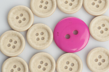 Fototapeta premium A single out pink button among white buttons,shot from top over a clear white surface