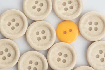 A single out yellow button among white buttons,shot from top over a clear white surface