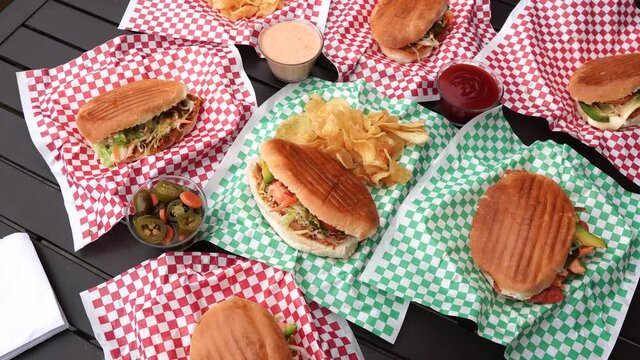 Overhead view of several delicious Mexican tortas with sauces and dressings, with a bowl of jalape&ntilde;o pepper and a torta in the middle accompanied by potato chips