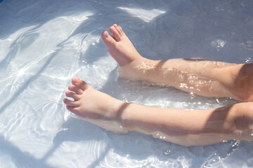 Feet of a child in the blue water of a children's pool. Fun summer outdoor activities, swimming and enjoying the water.