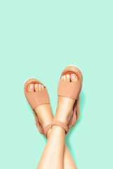 Female legs with white pedicure in summer brown sandals on background, copy space