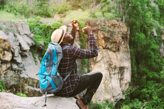 African man traveler sitting on the cliff and holding camera with backpack