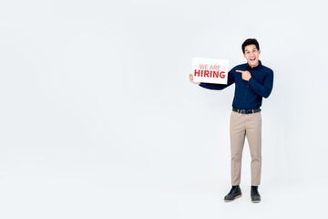 Portrait of smiling handsome Asian businessman holding and pointing to we are hiring sign in  isolated light gray background with copy space aside