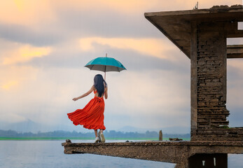 woman fashion dress standsing on the retro old cottage house in the lake, holding umbrella under raining season