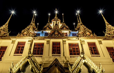 Golden shining Loha Prasat (Metal Castle) lit up at night, a pyramid shaped Buddhist temple from...