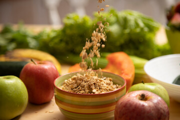 health concept granola falling into a colorful bowl with fruits and vegetables around