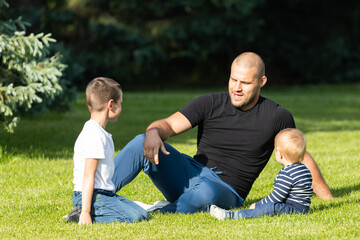 Happy young dad is playing with  her baby and son  in a park on a green lawn.Concept of a happy...