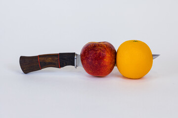 Hunting knife with a red Apple and orange on the blade on a white background, close-up.
