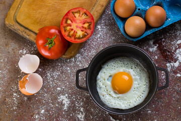 fried egg in a pan or pot accompanied by tomato and fresh eggs on a chopping board and flour