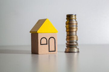 A wooden toy house with a yellow roof and a stack of coins.