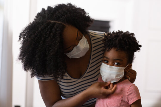 African American mother helping her daughter put on a face mask.