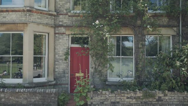 Beautiful entrance of a typical house in Cambridge city, england. The building has a nice red door, windows and plants hanging from the brick wall
