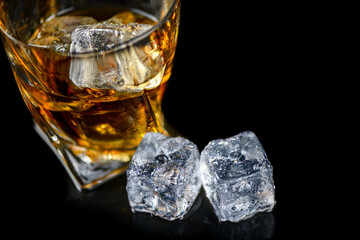Glass of whiskey with cube ice on black background