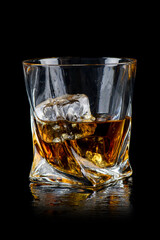 Glass of whiskey with cube ice on black background