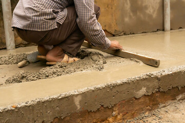 Indian construction worker levelling a cemented floor using wooden leveller manually, Stock image.