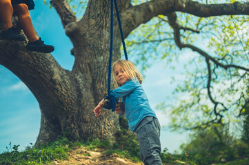 Naklejka na ściany i meble Preschooler resting on rope swing with his mother sitting in tree