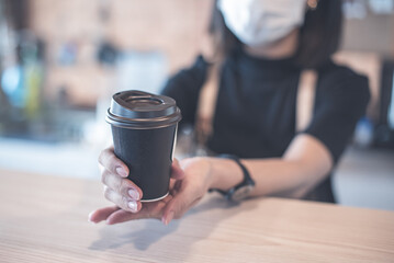 Barista  in apron and face mask standing  behind counter bar ready to give Coffee Service at the modern coffee shop, Modern cafe business, Social distancing concept. 