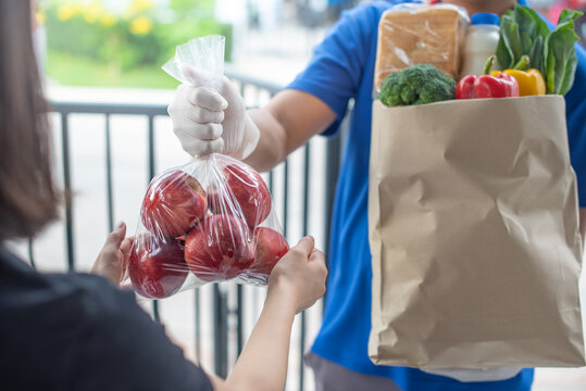 Deliver Man Wearing Medical Gloves And Face Mask In Uniform Handling Bag And  Parcel Box Give To Female Costumer Postman And Express Grocery Delivery Service During Covid19.