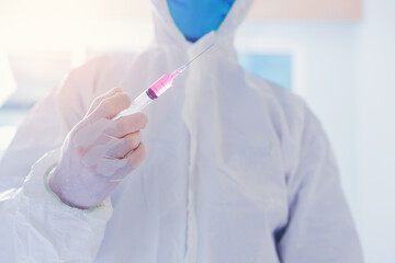Doctor in protective suit and face mask, holding syringe prepare for injects coronavirus, COVID-19 vaccine at bright room in hospital