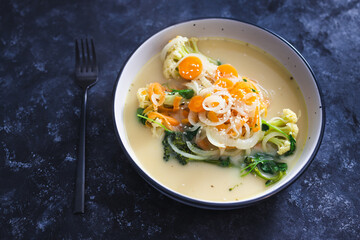 healthy plant-based food recipes concept, vegan soup with fresh veggies topping incuding caulini carrots onions and broccolini