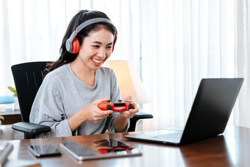 Funny Young woman wearing earphones playing computer game on laptop with joypad.