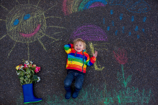 Cute toddler. playing in the rain with chalks, drawing on the asphalt, having fun