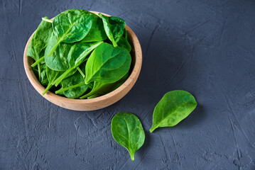 Fresh spinach leaves in wooden bowl on dark background. Organic food