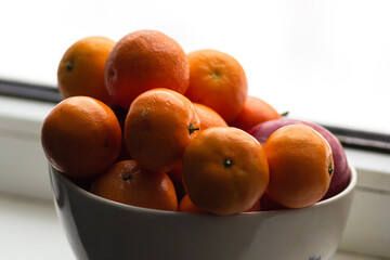 Bowl with tangerines on a window background