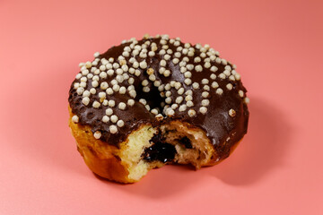 Bitten tasty chocolate donut on a pink background