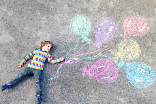 Kid boy having fun with colorful balloons drawing with chalks