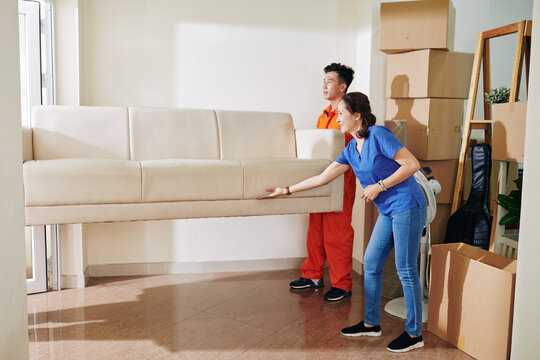 Mature Asian woman telling moving men where to put sofa they are carrying, horizontal shot, copy space