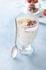 Glass of yogurt with banana and flax seeds on color background