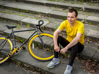 A young Man stopped to rest With his Bicycle in a public Park. He enjoys an early Sunny morning in the forest.