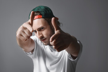 Naklejka premium Young man in a green baseball cap and white t-shirt pointing fingers at the camera with a confident expression, His facial expression is serious and intense, with a light beard and brown hair visible