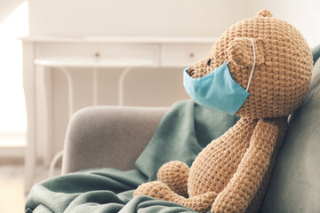 Teddy bear in medical protective mask on sofa in room