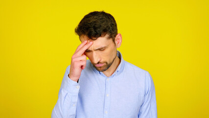 Handsome bearded man with a headache on a yellow background with copyspace. Pensive guy rested his fingers on his head