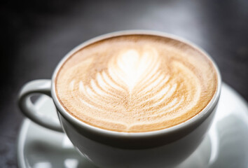 Latte art coffee in white cup on black desk with light from window , dark tone color