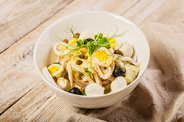 Salad with calamari, mozzarella cheese, olives, capers and microgreens in a white bowl. Mediterranean diet cuisine.. Close-up