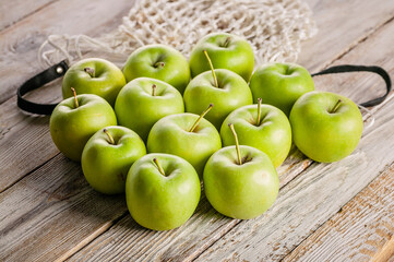 Juicy green apples and a cotton mesh bag on a wooden table. Close-up