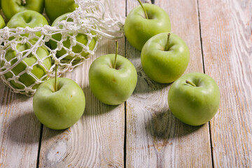 Close-up green apples and cotton string mesh bag on a wooden table. Copy space