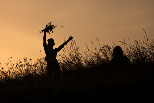 Silhouette of happy girl picking flowers during midsummer soltice celebraton against the background of sunset
