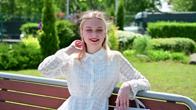 Video portrait of a happy caucasian girl with good make-up blonde smiling at the camera. Pretty woman posing in sunny weather in a park with a smile.