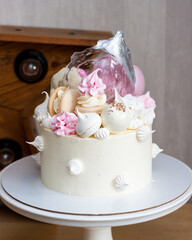 Elegant white cake with isomalt, chocolate, macaroons, meringues, pink and silver elements.