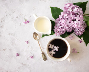 Fototapeta na wymiar Black coffee in a white cup and a milk jug with a lilac branch on a light background with space for text. Top view