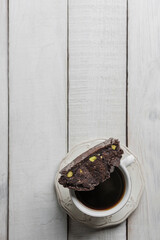 Top view of a cup of coffee with a Chocolate Biscotti or Cantuccini, on a rustic white wooden table with copy space.