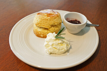 Close up butter scone with berries jam and clotted curd cream served on wooden table